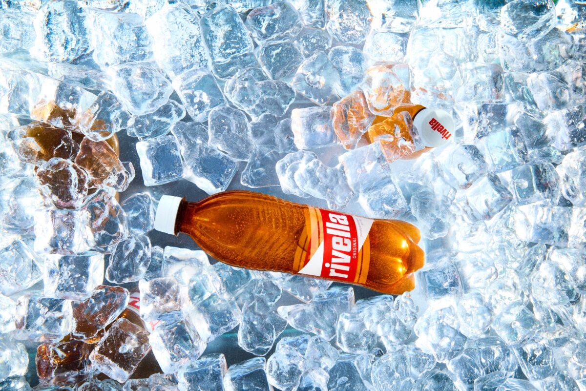 Rivella Rot Flasche inmitten von glitzernden Eiswürfeln platziert.