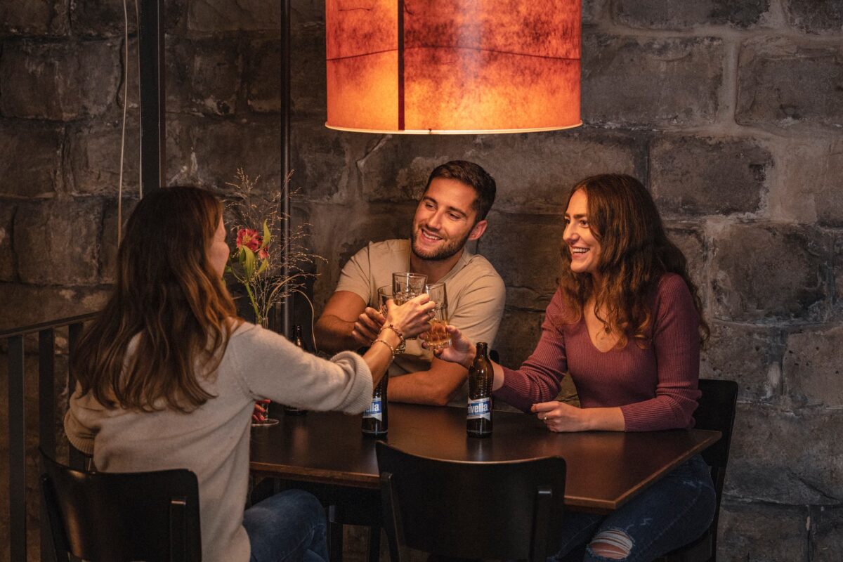 Abend-Stimmung, drei menschen sitzen an einem Tisch und stossen an mit rivella blau