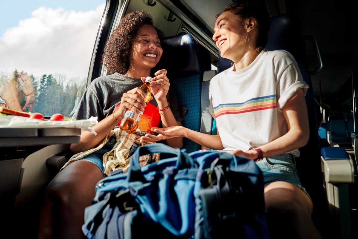 zwei fröhliche Menschen sitzen im Zug und drinken rivella.