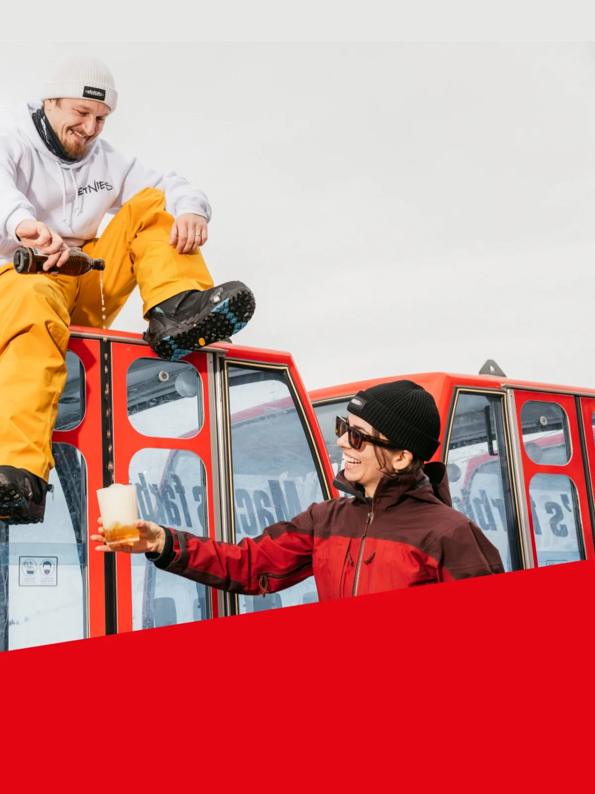 Zwei Personen geniessen Rivella auf roter Gondel im Schnee.