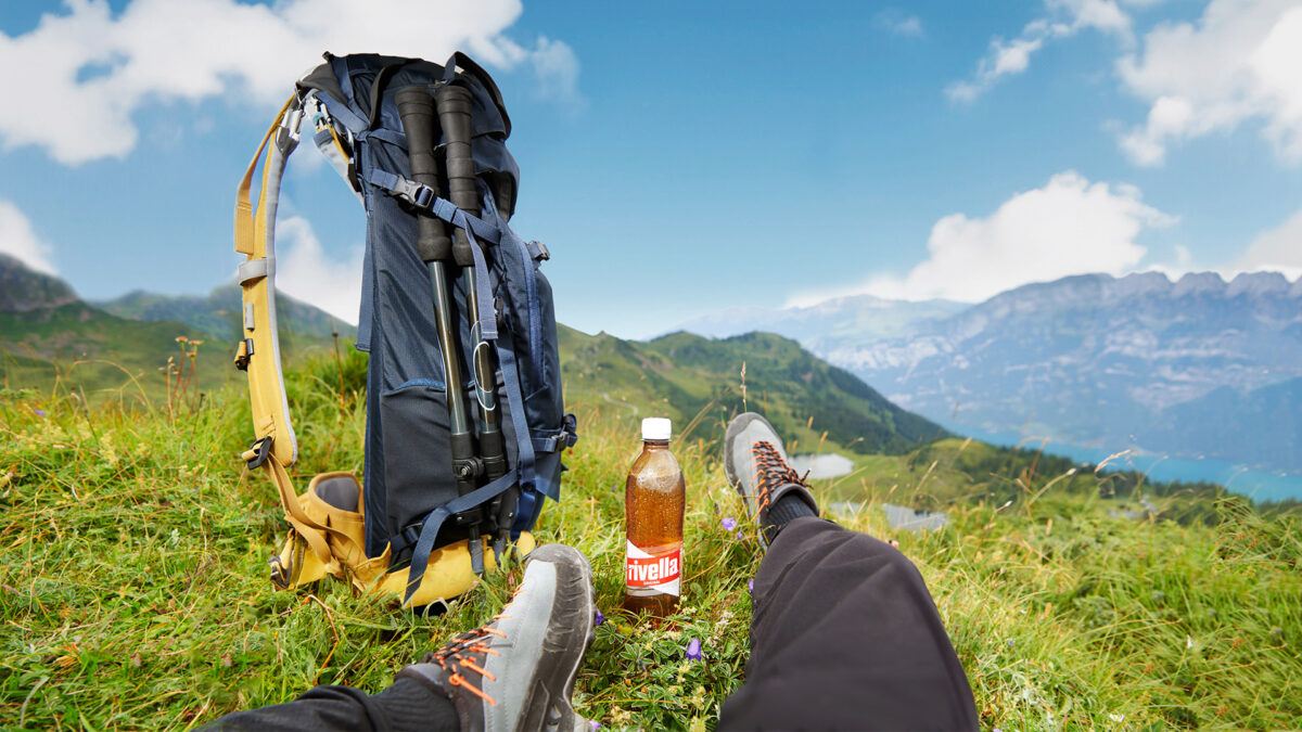 Wanderer entspannt mit Rivella Rot in alpiner Landschaft.