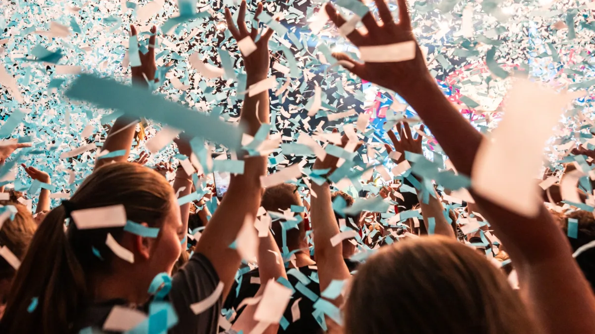 Jubelende Menschenmenge unter Konfettiregen auf lebendigem Event.