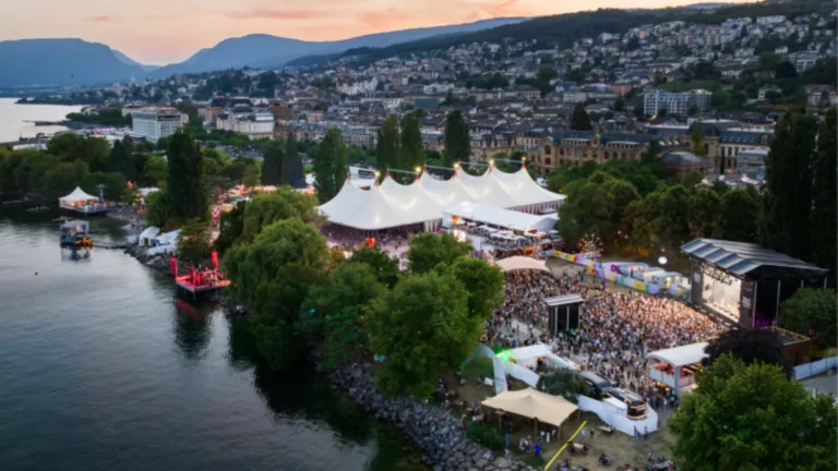 Großes Festzelt und Menschenmengen an einem See bei Sonnenuntergang.