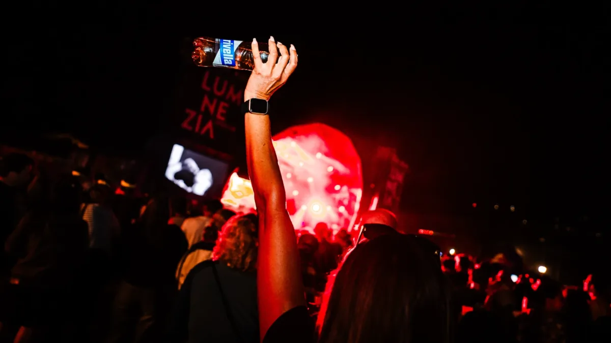 Person hält Rivella Blau Flasche während nächtlichem Festival in der Menge.