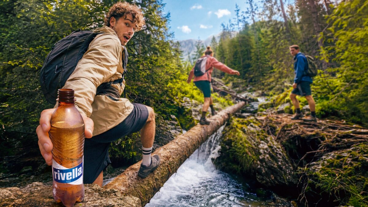 Person mit Rivella Zero Flasche beim Wandern über Baumstamm.
