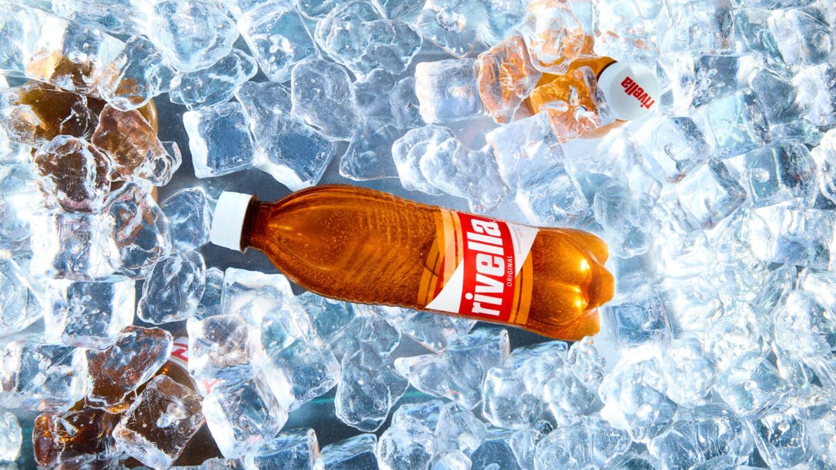 Rivella Rot Flasche liegt zwischen vielen Eiswuerfeln.