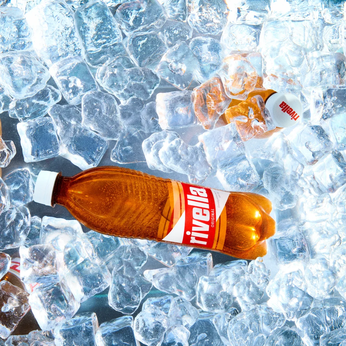 Zwei Rivella Original Flaschen eingebettet in Eiswürfel.
